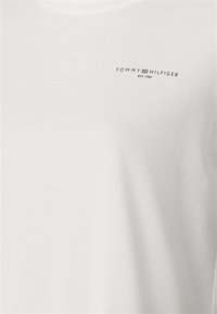 Biała bawełniana koszulka z okrągłym dekoltem. Posiada małe czarne logo "TOMMY HILFIGER EST. 1985" na lewej piersi. Miękka w dotyku.