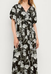 Maxi kjole i mørkegrøn med hvidt blomstermønster, med V-udskæring, korte puffærmer, indsnørret talje og flagrende nederdel.