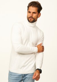 Weißer Rollkragenpullover aus einem weichen Material. Mit langen Ärmeln und gerippten Bündchen, kombiniert mit hellblauen Jeans.