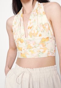 Blommönstrad crop top i mjuk tyg, med halterneck och en åtsittande midja. Färgerna inkluderar pastellrosa, grön och gul.