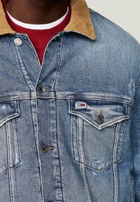 Jeansjacka med ljusblå tvätt, manchesterskinn i ljusbrun färg, två bröstfickor, kontrasterande sömmar och en logotypmärke på vänsterfickan.