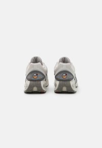 Scarpe da atletica bianche e grigie con una tomaia texture, tacco rotondo e ammortizzazione ad aria visibile, con un logo circolare sul retro.