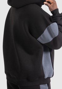 Schwarze Kapuzenpullover mit grauen Stoffakzenten an den Ärmeln; weicher Stoff und lockere Passform. Bündchen und Saum gerippt, einfaches Design.