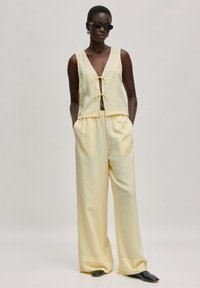 Lichtgele mouwloze top met een strikdetail aan de voorkant en bijpassende wijdlopende broek. Glad textuur, relaxte pasvorm en minimalistisch ontwerp.