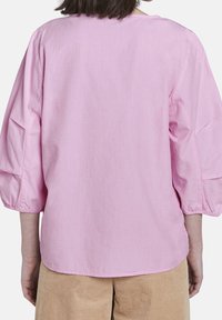 Maglietta rosa chiaro a maniche lunghe con una vestibilità comoda. Presenta maniche arricciate e un collo rotondo. Tessuto liscio con un design semplice e uniforme.