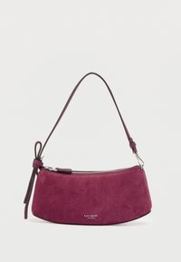 Sac à main en daim violet avec une forme courbée, une bandoulière en cuir et une fermeture éclair argentée. Nom de la marque « kate spade » affiché à l'avant.