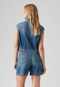Heledad denim overall-rammer kerge sinise pesuga, ilma varrukateta disainiga, nööpidega kinnitamine taljes ja tagakotid peente õmblustehnikatega.