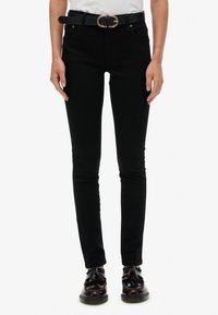 Vaqueros negros ajustados con cintura alta, detalles en los bolsillos y un cinturón negro con una hebilla ovalada dorada. Combinados con zapatos negros brillantes.