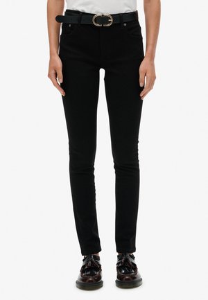Jean slim noir à taille haute, avec des détails de poches et une ceinture noire avec une boucle ovale dorée. Associé à des chaussures noires brillantes.
