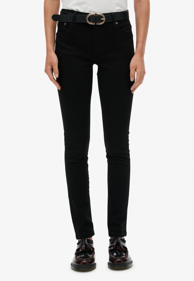 Vaqueros negros ajustados con cintura alta, detalles en los bolsillos y un cinturón negro con una hebilla ovalada dorada. Combinados con zapatos negros brillantes.