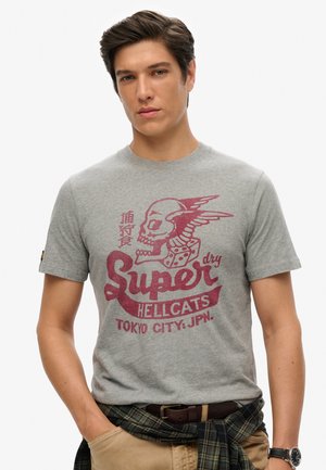 Grå kortærmet t-shirt lavet af bomuld med et rødt grafisk design med et kranium og vinger, tekst og terninger. Båret med ternet stof om livet.