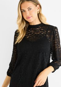 Black lace top with long sleeves, featuring a floral pattern and a high neckline. The fabric is textured with intricate designs.