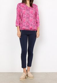 Lyserød bluse med V-hals og 3/4 ærmer, prydet med et blomsterdesign. Stylet med marineblå bukser og beige platform loafers.