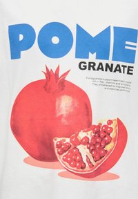 Hvid t-shirt med et stort rødt granatæblegrafik, med fed blå tekst der læser "POME" og sort tekst der siger "GRANATE."