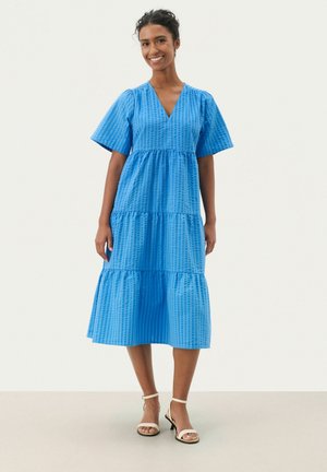Rochie albastră în straturi, cu decolteu în formă de V, mâneci scurte și țesătură texturată. Lungime sub genunchi, cu modele de grilă subtile și un drapaj moale.