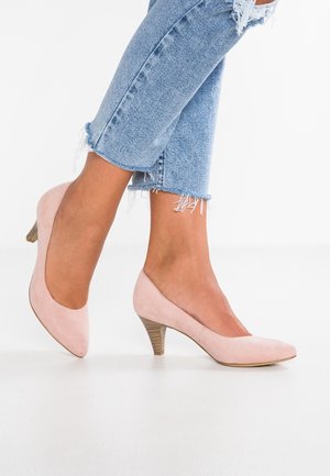 Vaaleanpunaiset mokkahuoneet, joissa on korkea kanta ja terävä kärki, yhdistettynä risasaumaisiin sinisiin farkkuihin.