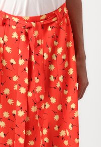 Rode bloemenrok met plooien, voorzien van gele bloemen en zwarte stelen. Inclusief een bijpassende riem en textuurstof.