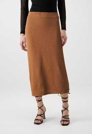 Bruine gebreide midi-lengte rok met een gestructureerde afwerking. Gecombineerd met zwarte gekruiste hoge hak sandalen. Minimalistisch en aansluitend ontwerp.