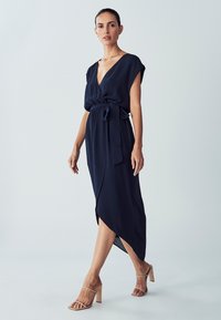 Námornícka obálková šaty s krátkymi rukávmi, viazaným pásom a vysokonízkym lemom. Vyrobené z hladkej látky s hlbokým výstrihom do V a minimalistickým dizajnom.