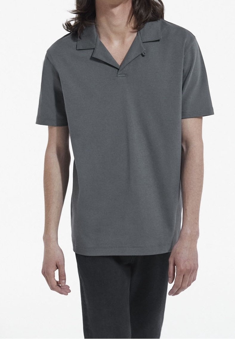 Personne portant un polo uni gris foncé à manches courtes et un pantalon noir sur fond blanc.