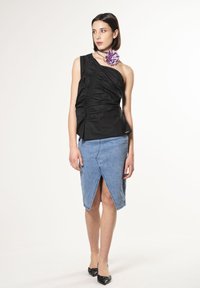 Zwarte one-shoulder top met ruches, gecombineerd met een lichtblauwe denim rok met een split aan de voorkant, aangevuld met een paarse bloemenaccessoire.
