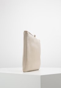 Pochette in pelle beige con texture liscia, forma rettangolare e chiusura superiore con zip. Presenta un design minimalista senza elementi hardware visibili.
