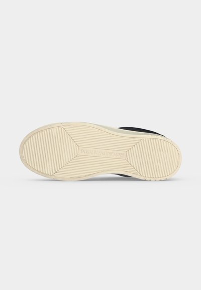 Semelle d'une basket noire avec une semelle extérieure en caoutchouc beige présentant un motif de bande de roulement linéaire et le nom de la marque embossé au centre.