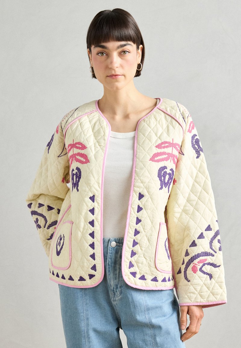 Quilted cream jacket with pink trim, featuring floral embroidery in pink and purple. Loose fit with two front pockets and geometric patterns.