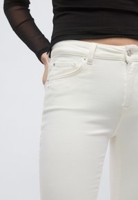 Τα λευκά τζιν από τζιν ύφασμα διαθέτουν εφαρμοστή σχεδίαση με ομαλή υφή, πέντε τσέπες και ασημένιο κουμπί στη ζώνη μέσης.