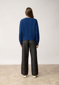 Naszywany niebieski sweter z okrągłym dekoltem, zestawiony z ciemnoniebieskimi dżinsami o wysokim stanie i szerokich nogawkach, z widocznym szwem i dwoma tylnymi kieszeniami.
