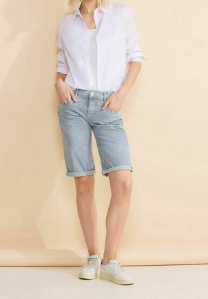 Shorts de mezclilla a rayas azules y blancas con dobladillos enrollados, combinados con una camisa blanca de botones ligera y zapatillas blancas informales.