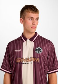 Koszulka polo w bordowo-kremowe paski, z krótkimi rękawami, kołnierzykiem oraz logo na lewej piersi. Materiał wydaje się gładki i lekki.