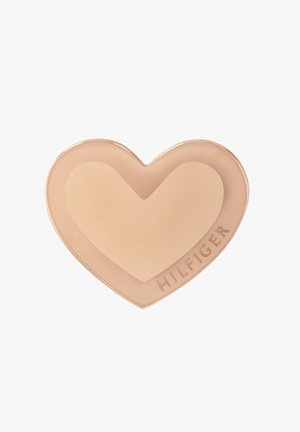 Producto de crema en forma de corazón de color beige claro, que presenta una textura suave. Logo "HILFIGER" grabado en el lado en un acabado contrastante.