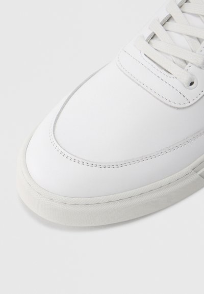 Λευκό δερμάτινο αθλητικό παπούτσι με λείο επάνω μέρος, στρογγυλή μύτη, και επίπεδη σόλα από καουτσούκ με ελάχιστες ραφές και υφασμένους λεπτομερείς.