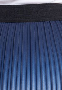 Gonna plissettata di un blu scuro, con un design testurizzato. Presenta una vita nera con la scritta "CARL LAGERFELD" in rilievo. Finitura in tessuto liscio.