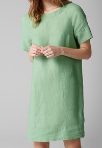 Grünes Leinenkleid mit kurzen Ärmeln, runder Halslinie und zwei aufgesetzten Taschen auf der Vorderseite. Hat eine lockere Passform und minimale Nähedetails.