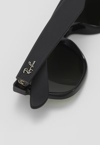 Occhiali da sole neri Ray-Ban con lenti tonde, finitura opaca e logo dorato sulla stecca. La montatura ha un design elegante e minimalista.
