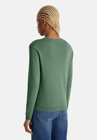 Zelený svetr s kulatým výstřihem a dlouhými rukávy, se strukturovaným pletením a žebrovanými manžetami, spárován s modrými džínami.