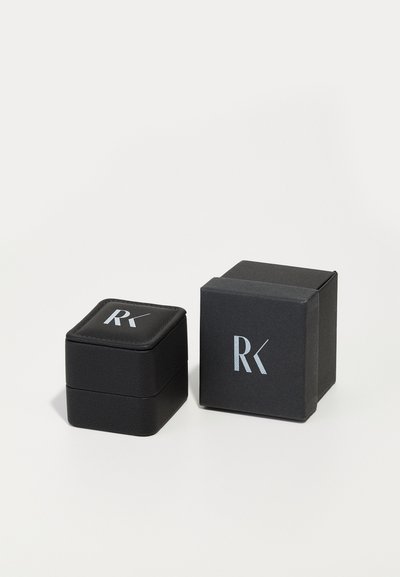 Cutii de bijuterii negre, una pătrată cu un capac căptușit și una cubică, ambele având logo-ul argintiu 'RK.' Exterior texturat, design elegant.