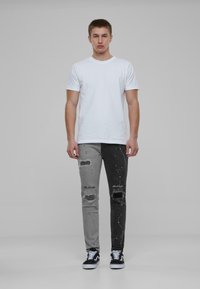 Smal Fit jeans med splittedesign; grå på den ene siden, svart på den andre. Slitt med hull og malingsprutdetaljer. Kombinert med en hvit t-skjorte.