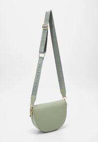 Zelená kožená přes rameno s zakřiveným tvarem, s logem vyraženým na šedém popruhu a zlatými kovovými akcenty.