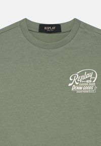 Olive zelené bavlněné tričko s kulatým výstřihem a krátkými rukávy. Na přední straně se nachází bílé potištěné logo. Měkká textura, volnočasový design.