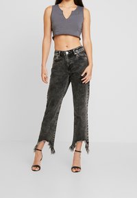 Top corto gris con un diseño de escote en V, combinado con jeans negros de tiro alto y desvanecidos, que tienen dobladillos deshilachados y un corte relajado. Tacones negros con tiras.