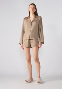 Braunes Satin-Pyjama-Set mit langärmliger Bluse und Shorts, ausgestattet mit einem Knopfverschluss und bequemer Passform; kombiniert mit hellen, flauschigen Hausschuhen.