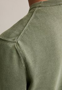 Khaki zielony sweter z teksturowanym wzorem dzianiny, z okrągłym dekoltem i widocznym szwem wzdłuż szwów oraz ramion.