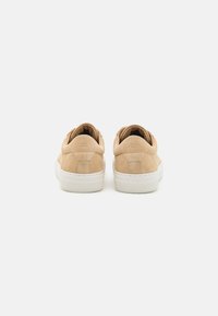 Beige suede sneakers with a low-top design, featuring a white rubber sole and minimalist stitching on the heel.