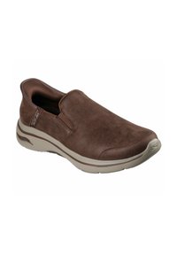 Chaussure marron à enfiler en daim souple avec un bout rond, des panneaux latéraux élastiques et une semelle en caoutchouc beige. Présente un logo discret sur le côté.