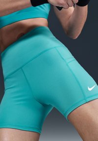 Turkise treningshorts laget av elastisk stoff, med høy midje, flate sømmer, og en liten hvit Nike-logo på siden.