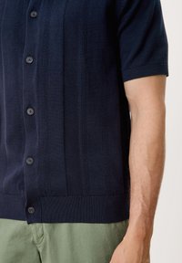 Marineblauw overhemd met korte mouwen en knopen, voorzien van verticale textuurstrepen, vijf knopen en ribgebreide manchetten en zoom. Van een katoenmix.