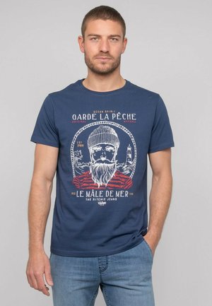 T-shirt en coton bleu marine avec un imprimé graphique blanc d'un pêcheur barbu, avec des accents rouges et du texte, col rond et manches courtes.